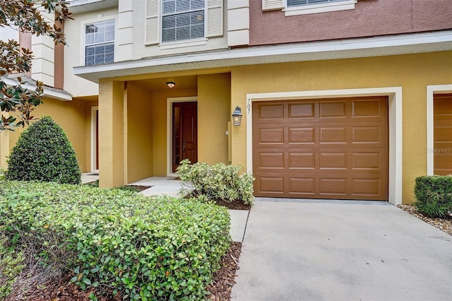 property entrance featuring stucco siding, an attached garage, and driveway