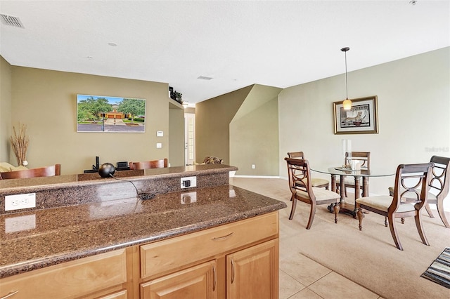 kitchen featuring light carpet, light brown cabinets, hanging light fixtures, light tile patterned floors, and dark stone countertops