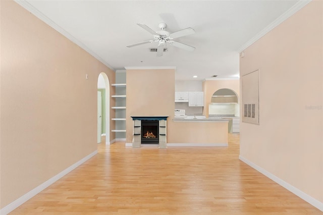 unfurnished living room featuring built in features, arched walkways, ceiling fan, light wood finished floors, and crown molding