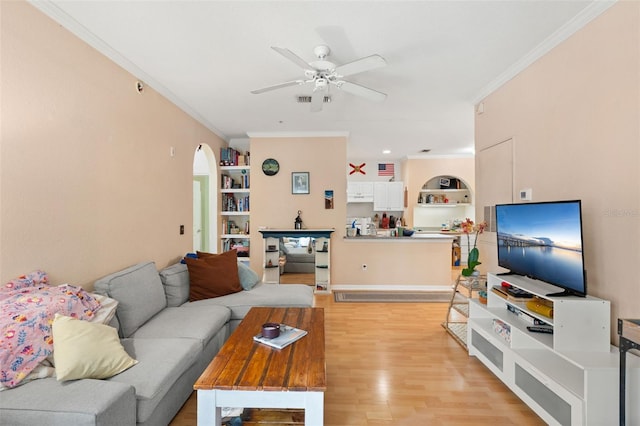 living room featuring ceiling fan, light wood-type flooring, crown molding, arched walkways, and built in shelves