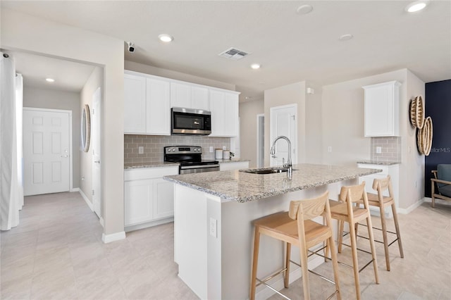 kitchen with appliances with stainless steel finishes, a sink, decorative backsplash, a kitchen island with sink, and baseboards