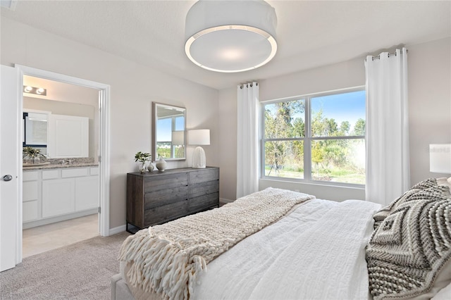bedroom with light carpet, ensuite bathroom, and baseboards