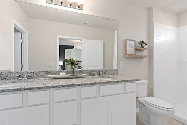 bathroom with toilet, double vanity, and a tile shower