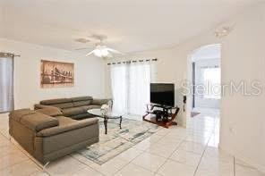 living room featuring healthy amount of natural light, tile patterned floors, ceiling fan, and arched walkways