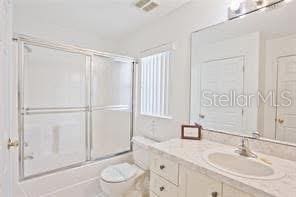 bathroom featuring bath / shower combo with glass door, toilet, and vanity