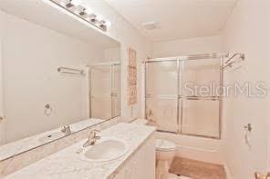 full bath with toilet, vanity, and bath / shower combo with glass door