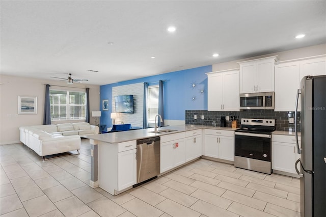 kitchen featuring appliances with stainless steel finishes, a sink, open floor plan, a peninsula, and tasteful backsplash