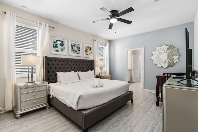 bedroom with light wood-style floors, baseboards, ensuite bath, and ceiling fan