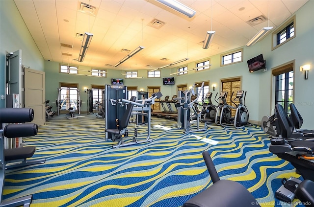 exercise room featuring carpet flooring, a towering ceiling, and baseboards