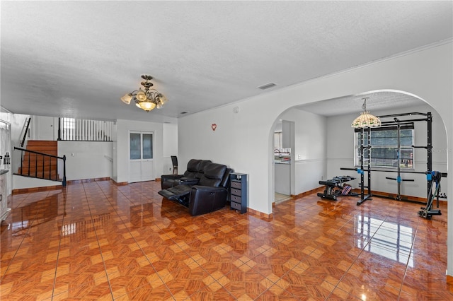 2500 Derby Dr, Kissimmee, FL 34744 - living room featuring arched walkways, a chandelier, a textured ceiling, baseboards, and crown molding