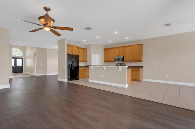 kitchen featuring black fridge, stainless steel microwave, open floor plan, baseboards, and light wood-type flooring