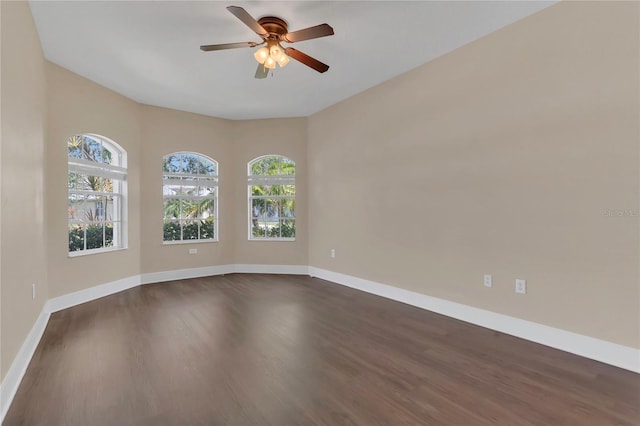 empty room with dark wood-style flooring, a ceiling fan, and baseboards