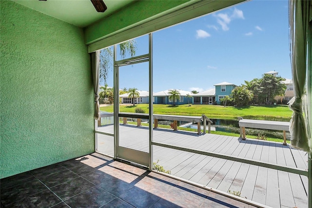 unfurnished sunroom with a ceiling fan, a water view, and a residential view