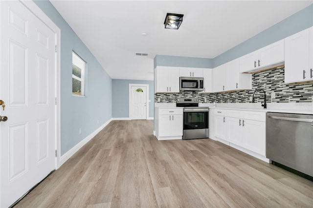 228 Ring Rd, Orlando, FL 32811 - kitchen featuring stainless steel appliances, tasteful backsplash, light countertops, light wood-style flooring, and white cabinets
