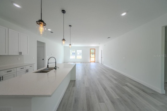 kitchen featuring a sink, open floor plan, white cabinetry, light wood-style flooring, and hanging light fixtures
