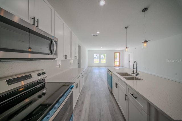 kitchen featuring stainless steel appliances, a sink, light wood finished floors, open floor plan, and white cabinetry