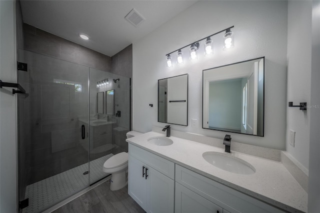 bathroom featuring toilet, a shower stall, double vanity, and wood finished floors
