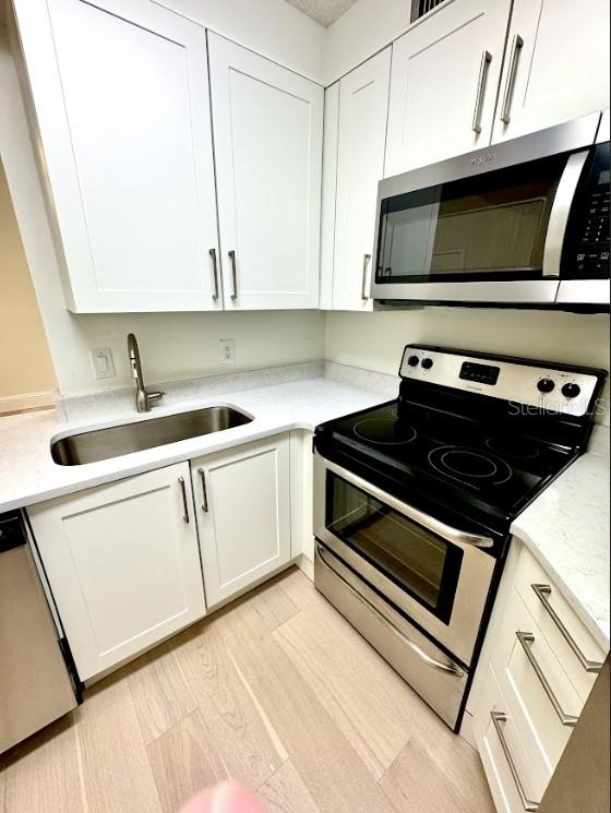 3621 Atrium Dr Unit U-4, Orlando, FL 32822 - kitchen with appliances with stainless steel finishes, a sink, white cabinets, and light countertops