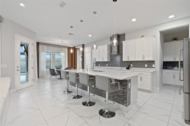 9845 Emerald Berry Dr, Winter Garden, FL 34787 - kitchen featuring wall chimney range hood, a sink, a kitchen breakfast bar, light marble finish floors, and stainless steel refrigerator