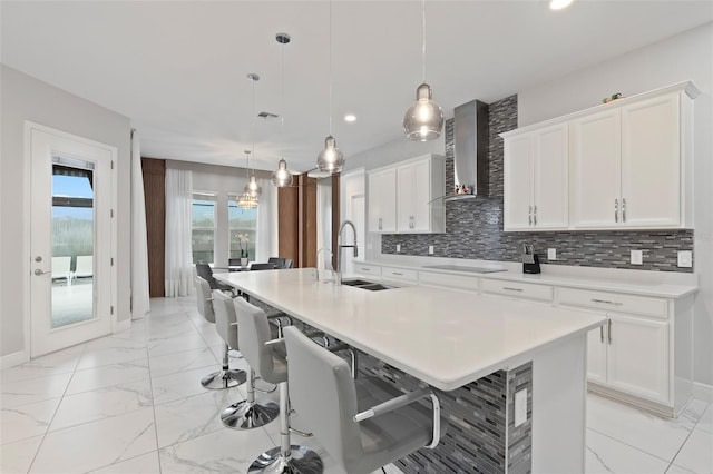 9845 Emerald Berry Dr, Winter Garden, FL 34787 - kitchen featuring a sink, wall chimney range hood, a breakfast bar area, tasteful backsplash, and light countertops