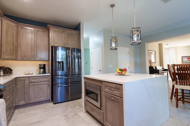 kitchen featuring appliances with stainless steel finishes, light tile patterned floors, light countertops, decorative light fixtures, and a center island
