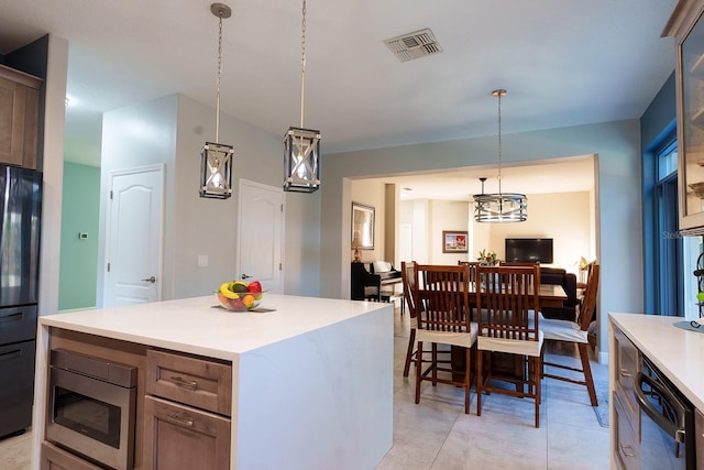 kitchen featuring light countertops, decorative light fixtures, freestanding refrigerator, a kitchen island, and dishwashing machine