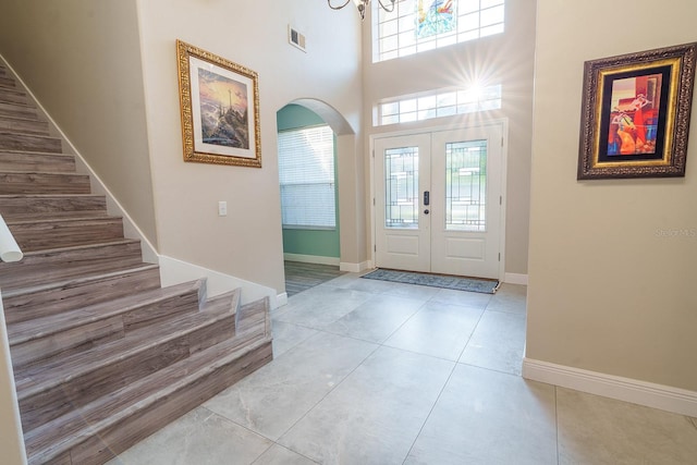 tiled entryway featuring stairs, arched walkways, a chandelier, french doors, and baseboards