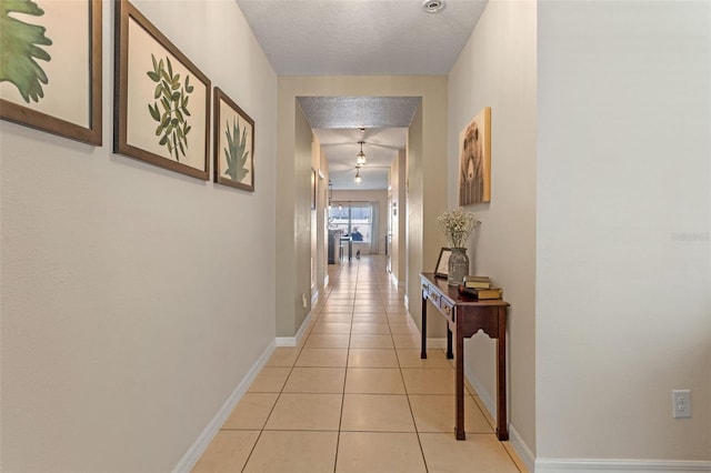 hall featuring light tile patterned flooring, baseboards, and a textured ceiling
