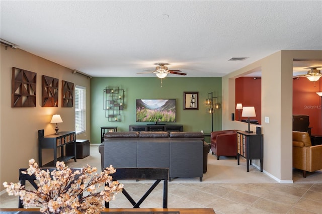 living room featuring ceiling fan, light colored carpet, a textured ceiling, baseboards, and light tile patterned floors