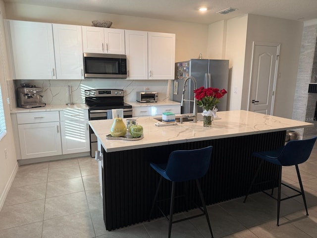 kitchen featuring appliances with stainless steel finishes, white cabinetry, a kitchen breakfast bar, and light stone countertops