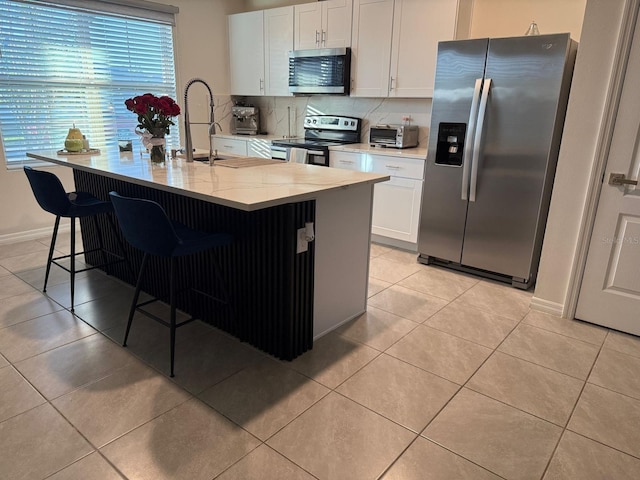 kitchen with stainless steel appliances, decorative backsplash, light tile patterned floors, white cabinets, and a kitchen breakfast bar