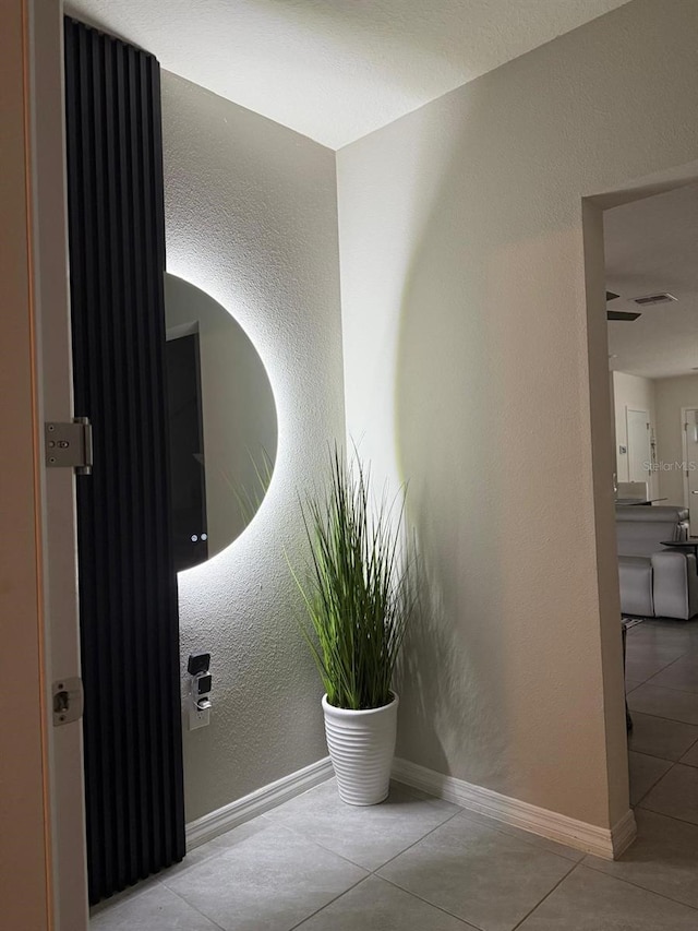 corridor with tile patterned flooring, a textured wall, and baseboards