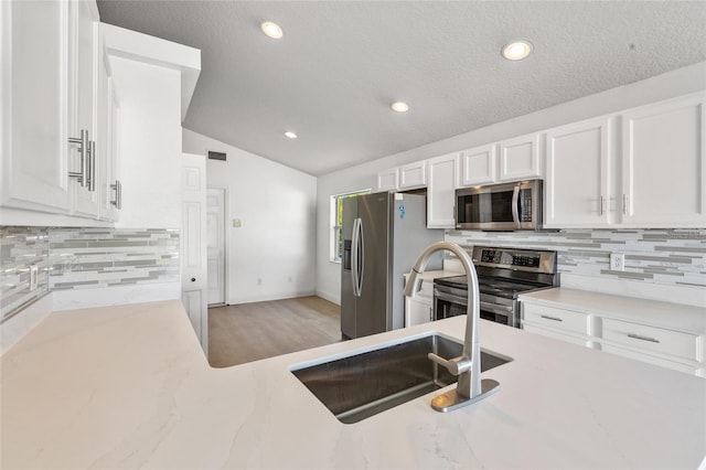 3078 Mandolin Dr, Kissimmee, FL 34744 - kitchen featuring appliances with stainless steel finishes, a sink, white cabinetry, vaulted ceiling, and light stone counters