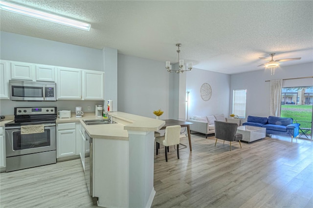 kitchen featuring appliances with stainless steel finishes, a peninsula, light wood-type flooring, a sink, and a textured ceiling