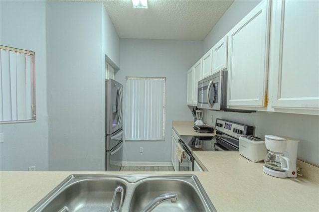 kitchen featuring stainless steel appliances, light countertops, a textured ceiling, white cabinets, and a sink