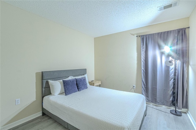 bedroom with wood finished floors, a textured ceiling, and baseboards