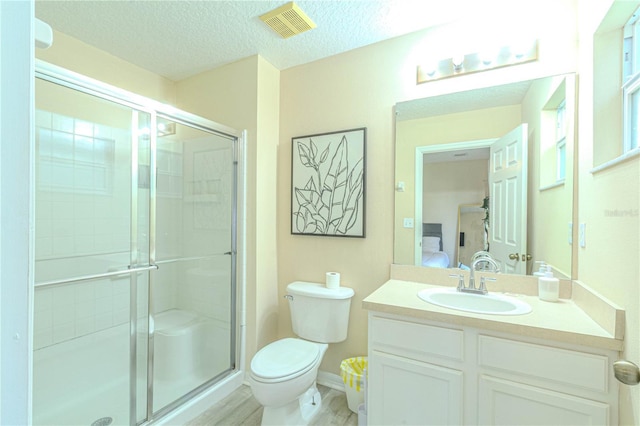 ensuite bathroom with a shower stall, toilet, vanity, a textured ceiling, and wood finished floors