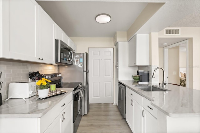 kitchen with stainless steel appliances, a sink, light wood-style flooring, backsplash, and white cabinets