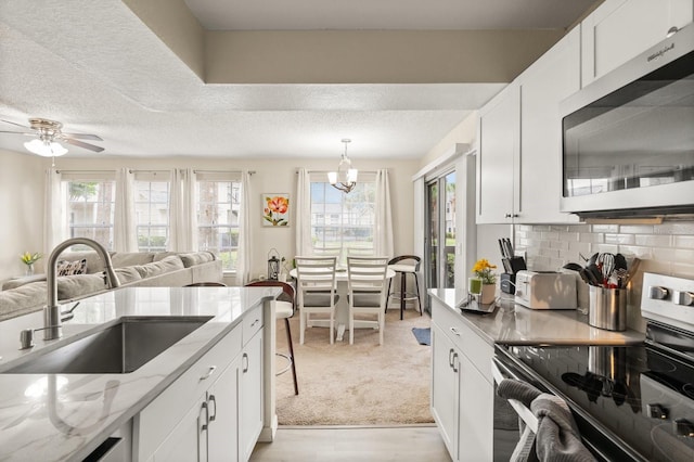kitchen with stainless steel appliances, a sink, white cabinetry, light stone counters, and a textured ceiling