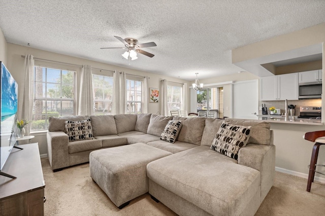 living room featuring ceiling fan, a chandelier, light colored carpet, a textured ceiling, and baseboards