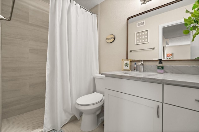 bathroom with toilet, vanity, a tile shower, and tile patterned flooring