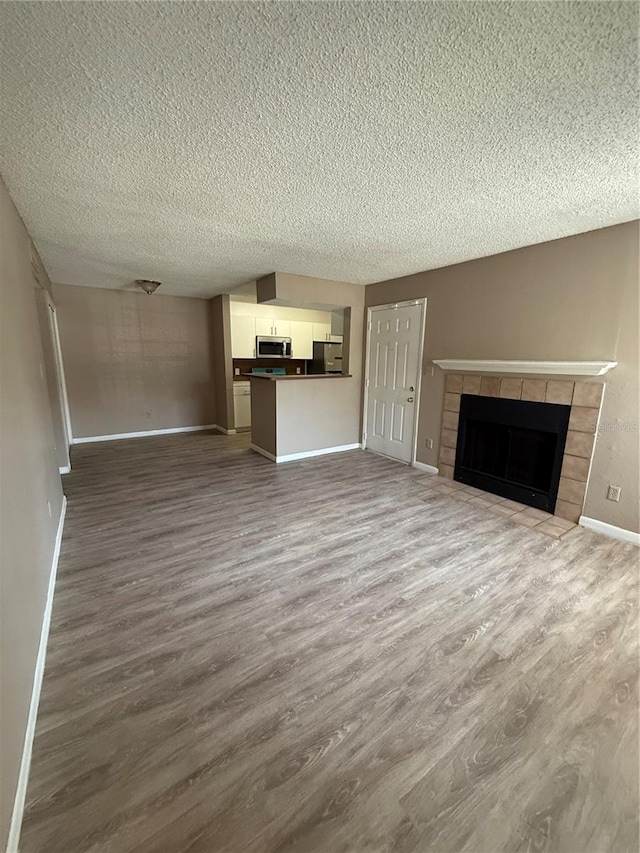 5540 Devonbriar Way Unit 103, Orlando, FL 32822 - unfurnished living room featuring dark wood-style floors, a textured ceiling, baseboards, and a tile fireplace