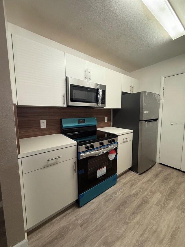 5540 Devonbriar Way Unit 103, Orlando, FL 32822 - kitchen featuring appliances with stainless steel finishes, light wood-style flooring, light countertops, white cabinetry, and a textured ceiling