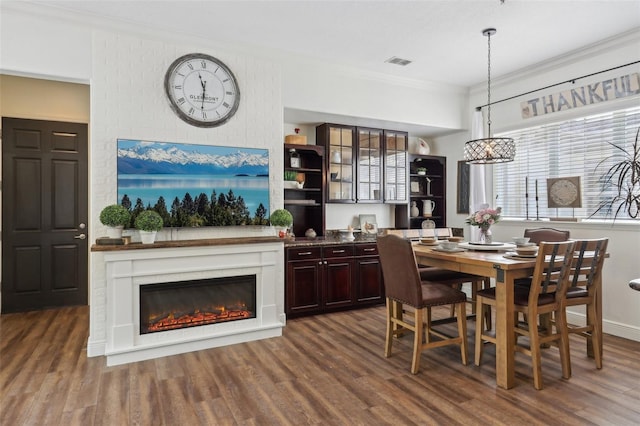 dining space with ornamental molding, dark wood-style floors, a large fireplace, and a chandelier
