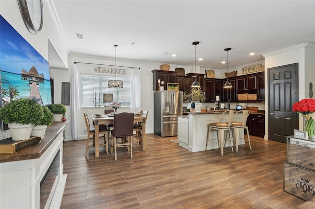 kitchen featuring stainless steel fridge, dark brown cabinetry, ornamental molding, wood finished floors, and a kitchen breakfast bar