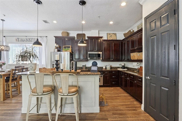 kitchen featuring stainless steel appliances, crown molding, a center island with sink, pendant lighting, and dark wood finished floors