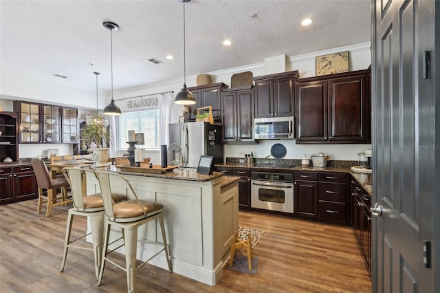 kitchen with appliances with stainless steel finishes, a breakfast bar area, a center island with sink, light wood-type flooring, and dark stone countertops