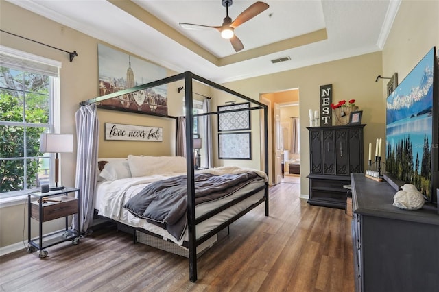 bedroom with a raised ceiling, wood finished floors, ensuite bath, baseboards, and crown molding
