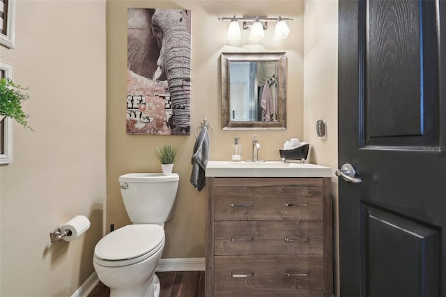 half bath featuring baseboards, toilet, vanity, and wood finished floors