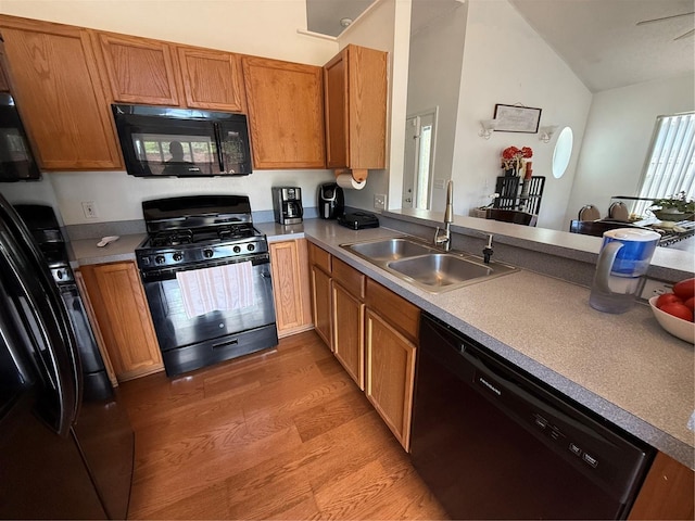 kitchen with black appliances, a sink, vaulted ceiling, light wood-style flooring, and brown cabinets